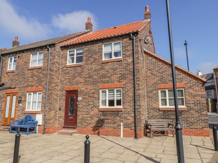 A brick semi detached house with red tiled roof and wooden benches outside at Abrahams Cottage in Whitby