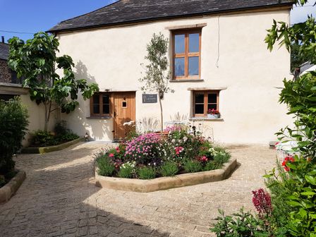 A courtyard with a flower bed in front of a cream building with wooden windows and door at Badharlick Granary in Elgoskerry