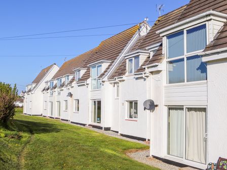 A row of white houses with brown roofs and large windows next to a grassy area at Isallt Cove in Trearddur Bay
