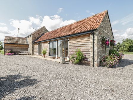 An exterior view of a stone and wood barn with a tiled roof and flower pots around Golden Valley Barn Oldbury-On-Severn