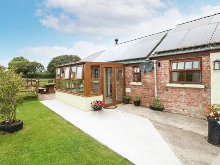 A brick house with solar panels on the roof and a wooden patio enclosure next to a grassy lawn at The Old Farm Shop in Narberth