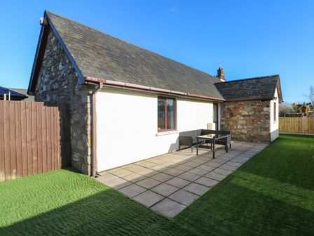 An outdoor patio area with tiled floor artificial grass seating and stone and white walls at The Old Well Bungalow - Ty Mawr Farm in Cardiff