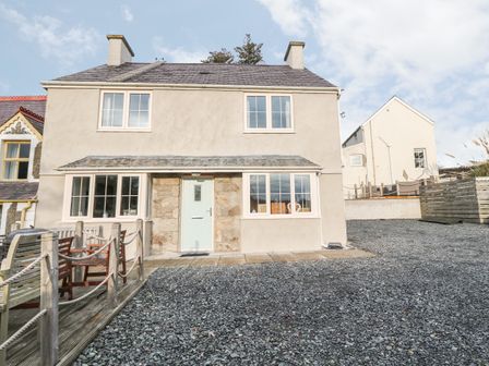 A two story house with multiple windows a light blue door and a gravel driveway at Castell in Abersoch