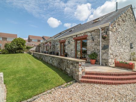 A stone barn conversion with glass doors and brick steps leading to a patio and lawn at Woodside Barns in St Austell