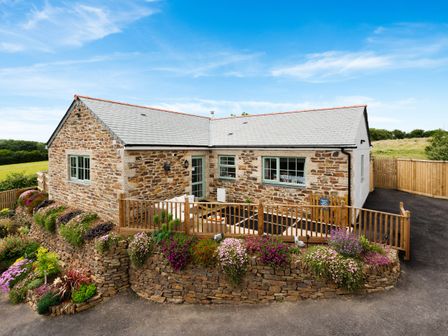 Stone cottage with grey roof and wooden fence surrounded by flower beds at Bear Cottage in Chacewater near Truro