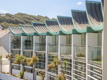 A modern building with curved green roofs and glass balconies with plants outside at The Lookout in Westward Ho