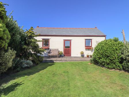A small house with a red door and two windows with potted plants on a patio and a lawn in front at Bowling Green Cottage in Carnkie near Camborne