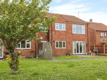 A backyard with a tree and grass in front of a two-story brick house with multiple windows and a patio at Sea-u-Soon in Runswick Bay