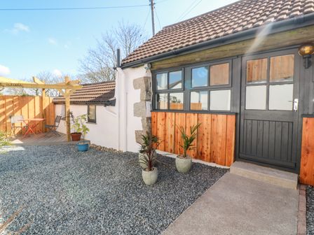 An outdoor area with black stone ground covering a small patio with a table and two chairs a building with black framed windows and door at Toadstools in Rame Cross near Penryn