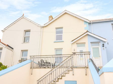 Exterior of a two-story house with a staircase leading to a wooden deck and white front doors at Quayside View in Brixham