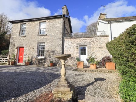 A stone cottage with a red door gravel driveway stone birdbath and potted plants at Westmorland Cottage in Grange-Over-Sands