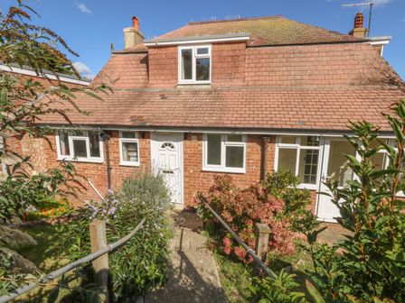 A brick house with a tiled roof and white doors and windows surrounded by a garden with plants and shrubs at Thorncroft in West Bay