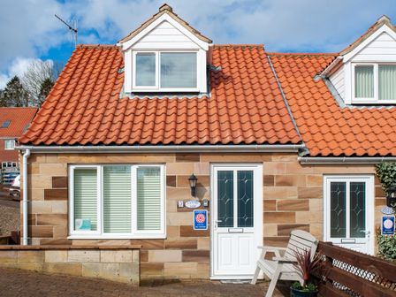 A cottage with red tile roof white doors and windows and a wooden bench outside at Estuary View in Whitby