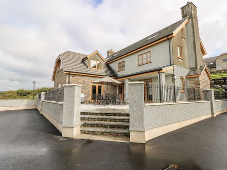 An outdoor patio area with table chairs umbrella and grill next to a two story house at Grooms Quarters at Pant y Gaseg Farm in Ammanford