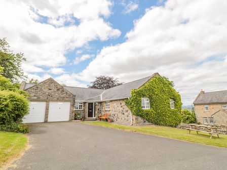 A stone house with ivy on one side a driveway and garage doors at Coquet View Cottage in Rothbury