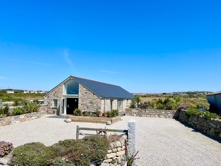A stone building with a slate roof and gravel courtyard surrounded by stone walls and plants at See Two Seas Cape Cornwall in St Just