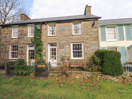 Stone exterior of a terraced house with white framed windows and doors small garden with bushes and a wooden bench at Brackenbury Cottage in Beddgelert
