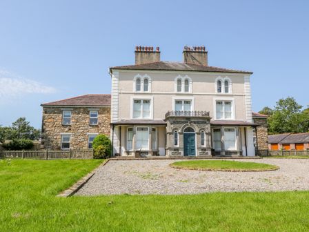 A large house with stone and white walls a gravel driveway and green grass at Tirionfa in Llangefni