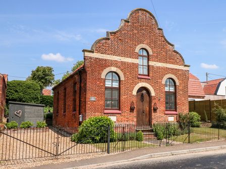 A red brick building with arched windows a wooden door and small fenced garden at The Old Chapel in Flitcham