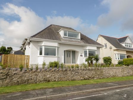 A white detached house with a stone wall and small plants in front at Y Gogarth in Benllech