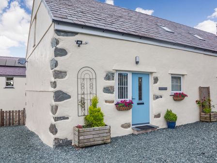 A cottage with a blue door stone walls and flower planters at Marchlyn in Deiniolen