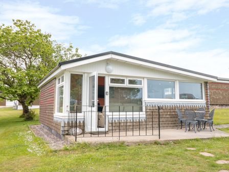 A single-story house with large windows and an outdoor patio with metal table and chairs at 201 Norton Park in Dartmouth