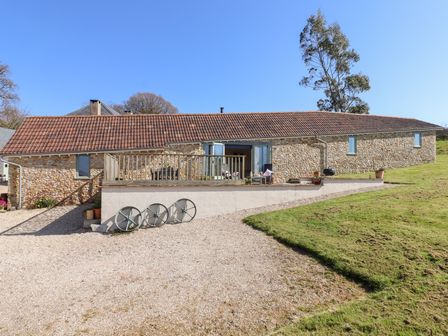 An exterior view of a stone building with a tile roof and a wooden railing on a raised patio at The Shippon at Wyke Farm in Lyme Regis