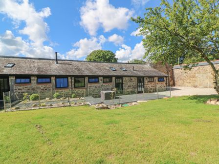 A stone building with multiple windows and a glass fence in front of a grassy yard at Nanas Cottage in Praze-An-Beeble