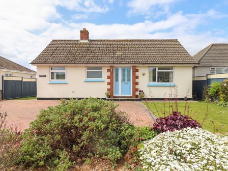 A bungalow with blue door and windows surrounded by bushes and flowers at Tremethic in Trewoon