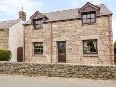 Stone cottage with two dormer windows and a stone wall in front at Mossley Cottage in St Buryan