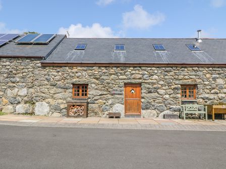 A stone house with a wooden door and two windows with flower boxes beside a paved road at Craig Y Deryn Bryncrug near Tywyn