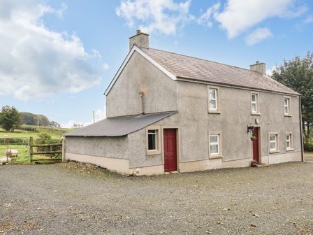 A two-story farmhouse with red doors and gravel driveway with fields and sheep in the background at Shaws Hill Farmhouse in Kells County Antrim