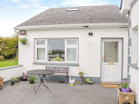 An outdoor patio with a round table bench flower pots and a white door at Sunset View in Keelogues near Glenamaddy County Galway