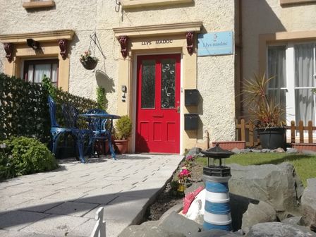 An outdoor patio area with a red door and blue chairs at Llys Madoc in Penmaenmawr