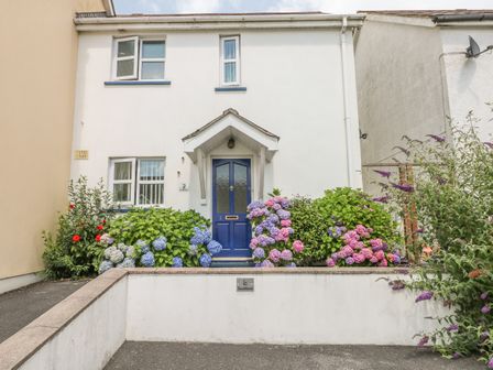 A white two-story house with a blue front door and flowering bushes in front at 2 Primrose Cottage Saundersfoot