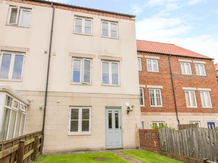 The rear view of a three story house with multiple windows a light blue door a grassy yard and wooden and brick fencing at Tides Reach Whitby