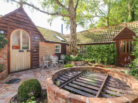 A brick courtyard with metal grate fire pit white metal chairs and wooden doors at The Hemmel in Faringdon