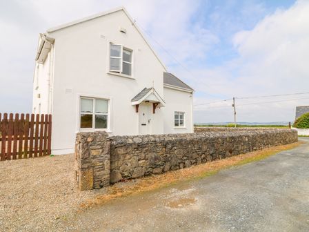 A white house with a stone wall and a wooden gate on a gravel driveway at Doornogue in Churchtown near Fethard-on-Sea