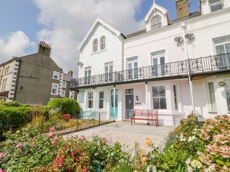 The exterior of a white two-story house with a balcony and a garden with flowers and bushes at Mor Awel in Beaumaris