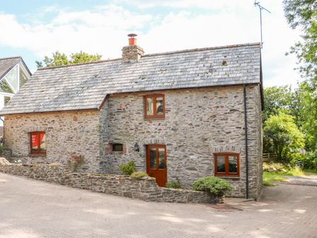A stone cottage with a tiled roof and wooden framed windows at Great Bradley Cottage in Withypool