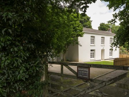A white two-story house behind a wooden gate with trees around at 9 Copes Gardens in Truro