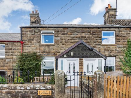 The exterior of a stone cottage with two white front doors a black metal gate and wooden bench at Hart Cottage in Glaisdale