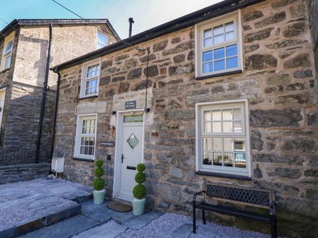 Stone front exterior of a house with white framed windows a white door two potted topiary plants and a black bench at Yr Hen Dy Capel in Blaenau Ffestiniog