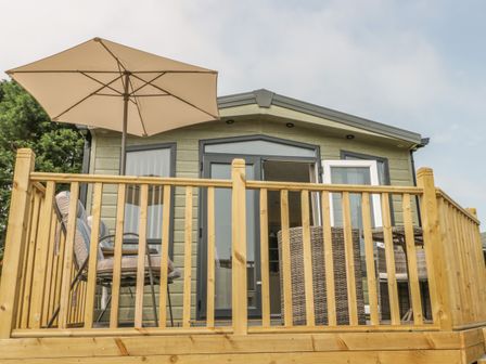 A wooden deck with outdoor chairs umbrella and table outside a small building at The Sequoia in Cloughton