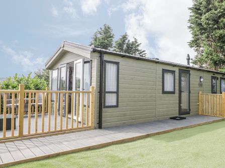 A small house with a wooden deck and railing surrounded by trees at The Maple in Cloughton