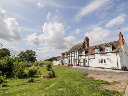 A large farmhouse with a garden and grass lawn under a partly cloudy sky at The Farmhouse in Ledbury