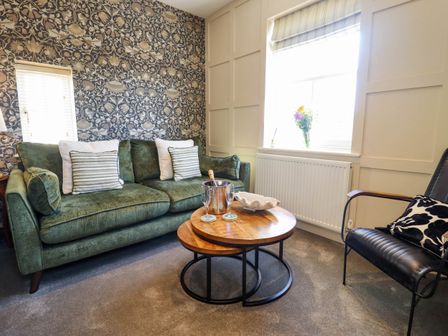 A living room with a green sofa cushions and a wooden nesting coffee table with a champagne bucket at Gavel Cottage in Whitby