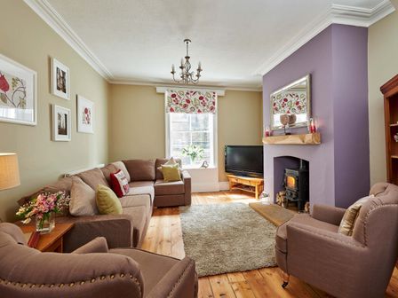A living room with a sofa and armchairs around a fireplace with a television on a stand at Harbour House in Whitby