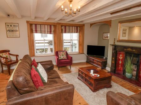 A living room with a brown leather sofa a red armchair a wooden coffee table a TV on a wooden stand and a fireplace at Foresters House in Whitby