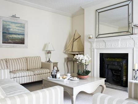 A living room with striped sofas a white coffee table with tea and scones a decorative sailboat on a side table and a fireplace with a large mirror above at Albany House Whitby